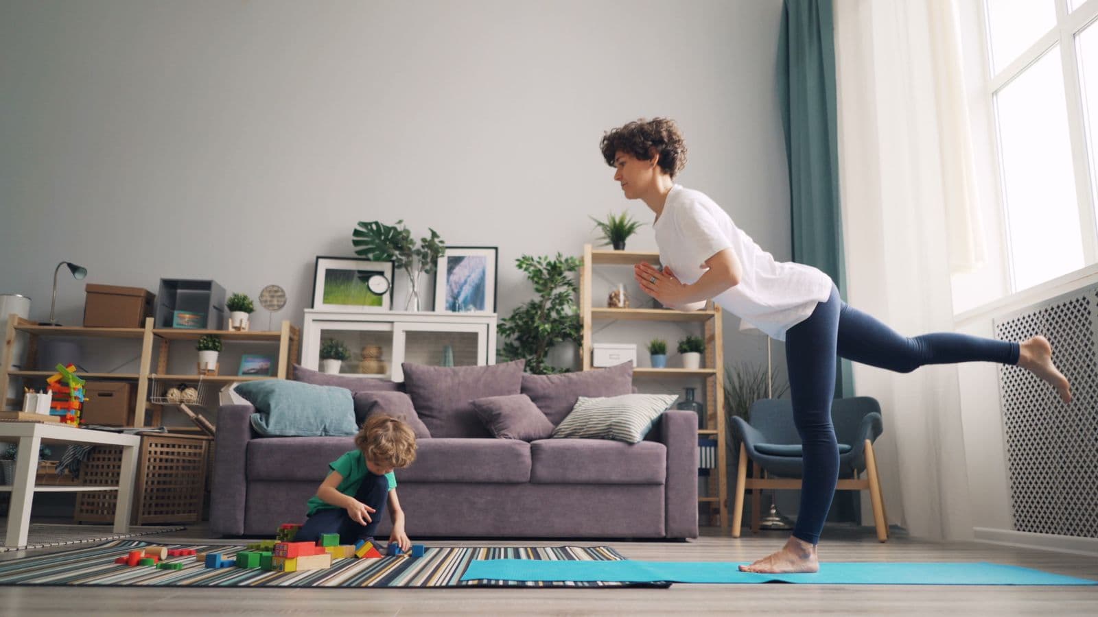A mum exercising in her living room while her young son plays with blocks
